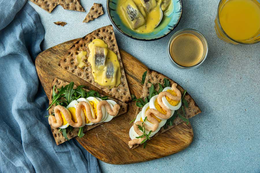 
Schwedische Mahlzeit. Knäckebrot mit verschiedenen Belägen: eingelegter Hering in Senfsauce, Ei, Rucola und Kabeljaurogenpaste