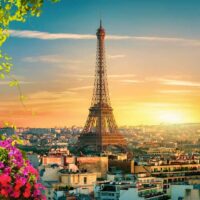 Der Eiffelturm Paris bei Sonnenuntergang, beleuchtet in goldenem Licht mit der Pariser Skyline im Hintergrund