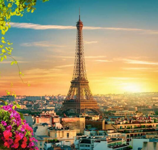 Der Eiffelturm Paris bei Sonnenuntergang, beleuchtet in goldenem Licht mit der Pariser Skyline im Hintergrund