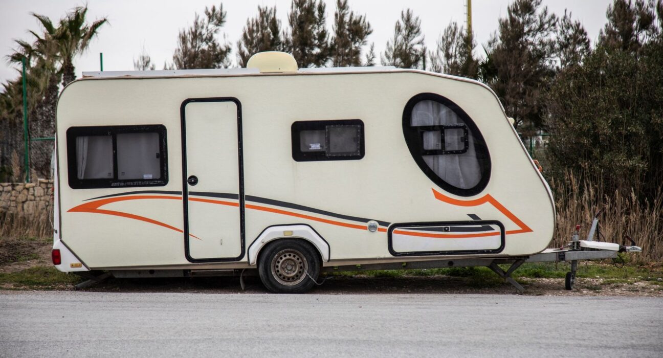 Auto mit Wohnwagen fährt auf einer Autobahn durch hügelige Landschaft