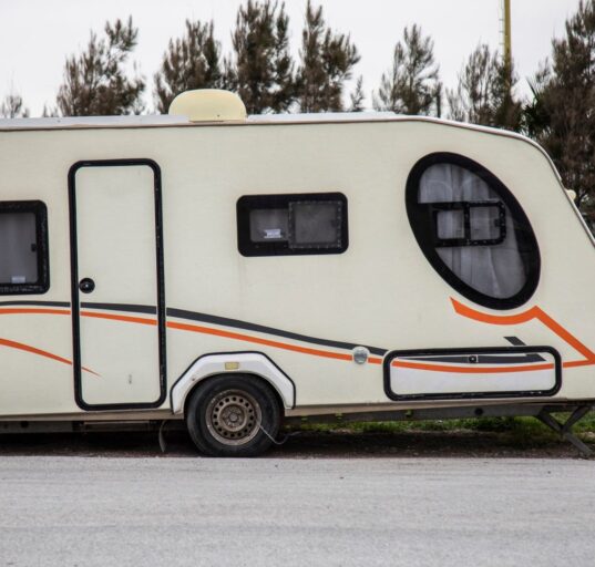 Auto mit Wohnwagen fährt auf einer Autobahn durch hügelige Landschaft