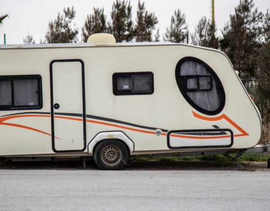 Auto mit Wohnwagen fährt auf einer Autobahn durch hügelige Landschaft
