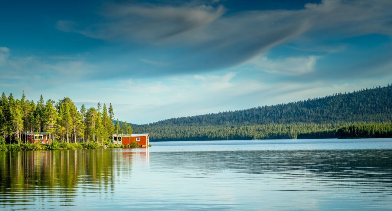 Campingplatz an einem schwedischen See mit rotem Holzhaus und Wald
