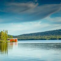 Campingplatz an einem schwedischen See mit rotem Holzhaus und Wald