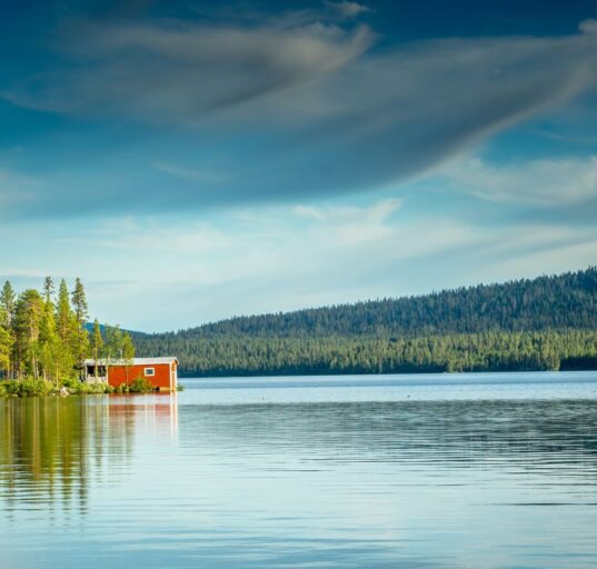 Campingplatz an einem schwedischen See mit rotem Holzhaus und Wald