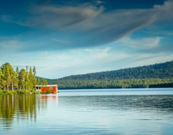 Campingplatz an einem schwedischen See mit rotem Holzhaus und Wald