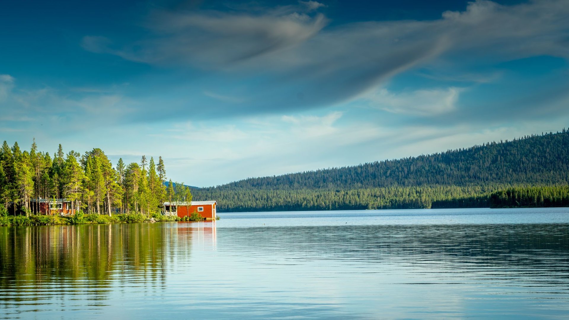 Campingplatz an einem schwedischen See mit rotem Holzhaus und Wald