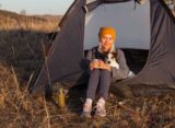 Frau mit Hund sitzt mit einer Tasse vor ihrem Zelt in der Abendsonne