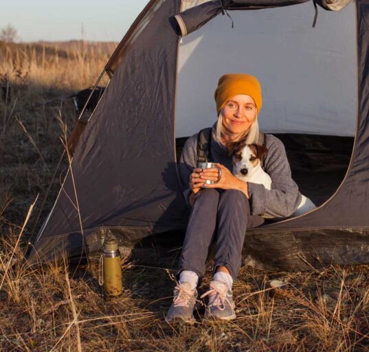 Frau mit Hund sitzt mit einer Tasse vor ihrem Zelt in der Abendsonne