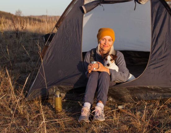 Frau mit Hund sitzt mit einer Tasse vor ihrem Zelt in der Abendsonne