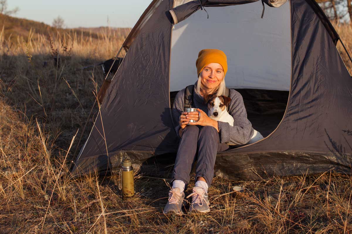 Frau mit Hund sitzt mit einer Tasse vor ihrem Zelt in der Abendsonne