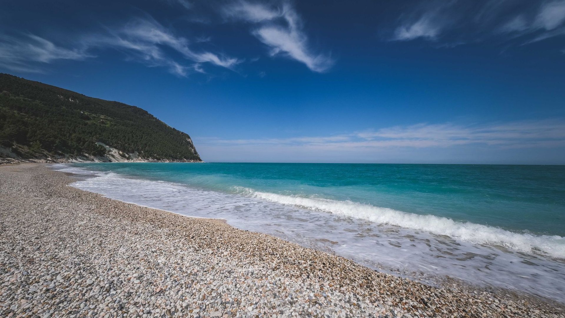 Kiesstrand mit klarem Wasser vor bewaldeten Bergen