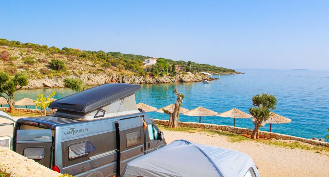 Campingbus an einer Bucht mit Sonnenschirmen am Mittelmeer