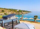 Campingbus an einer Bucht mit Sonnenschirmen am Mittelmeer