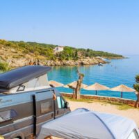 Campingbus an einer Bucht mit Sonnenschirmen am Mittelmeer