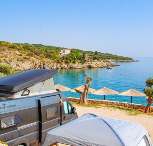 Campingbus an einer Bucht mit Sonnenschirmen am Mittelmeer