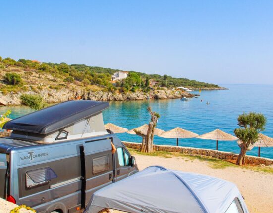 Campingbus an einer Bucht mit Sonnenschirmen am Mittelmeer