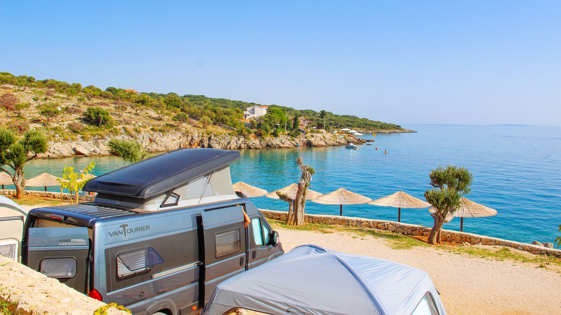 Campingbus an einer Bucht mit Sonnenschirmen am Mittelmeer
