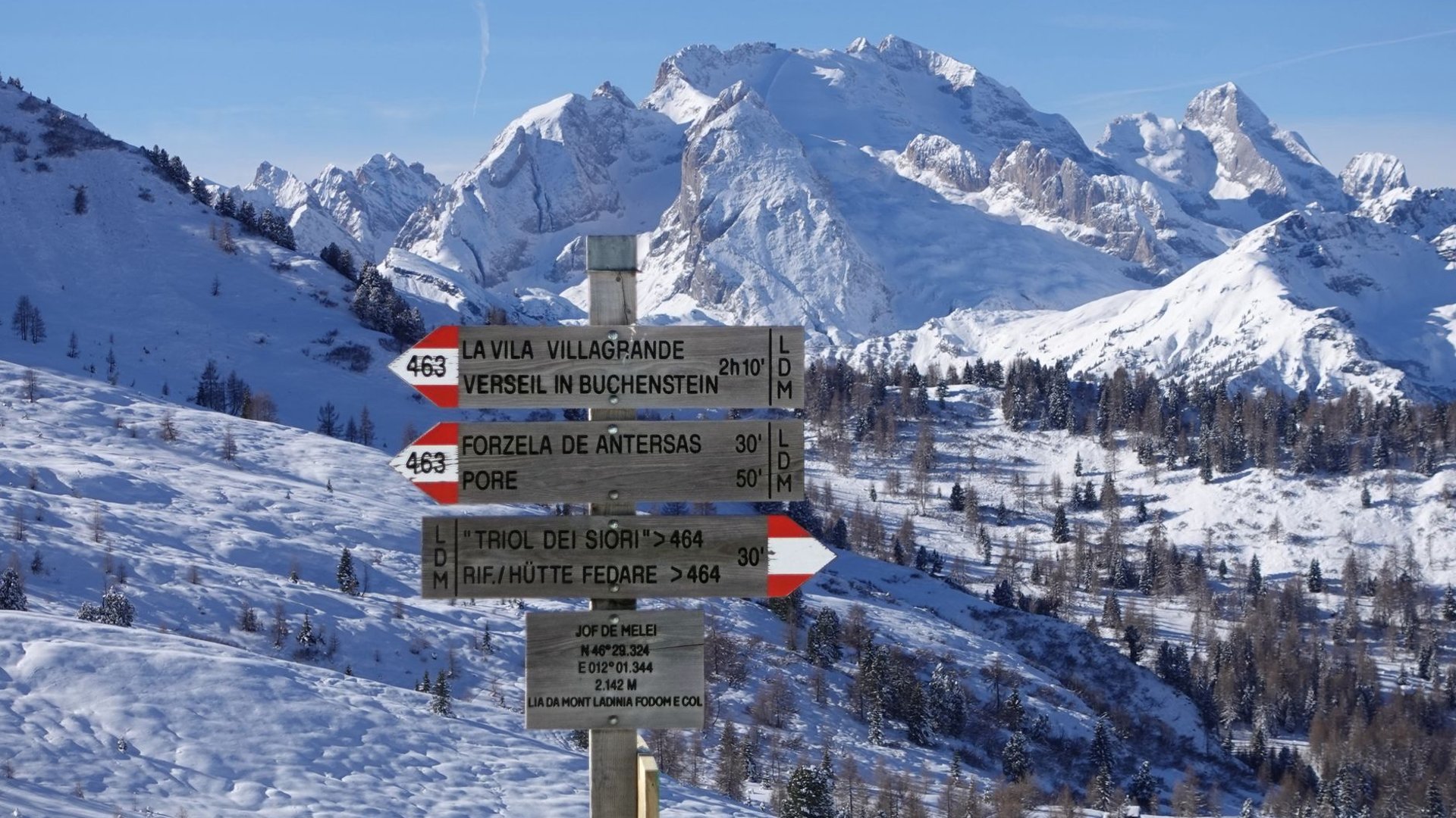 Wegweiser an einem Bergweg vor verschneiten Gipfeln
